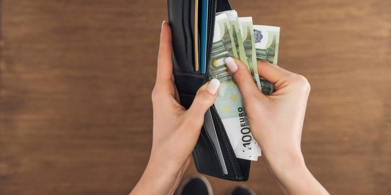 top view of woman putting euros banknotes in wallet on wooden background